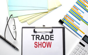 clipboard with paper that says "trade show" surrounded by graphs and glasses